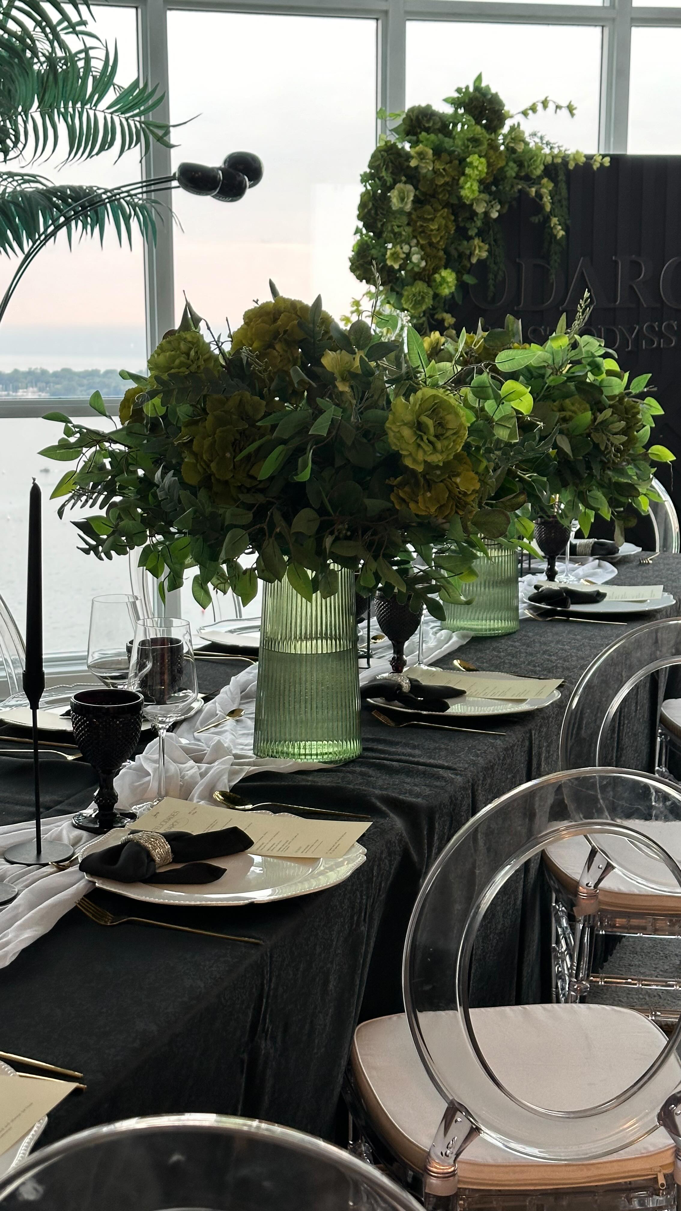 Moody dinner table setting with black linens, candlelight, and a sculptural white floral centrepiece.