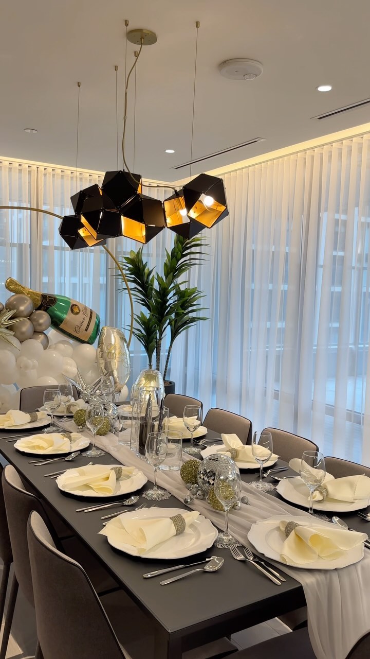 New Year’s Eve dinner table with gold place settings, candles, greenery, and coordinated balloons.