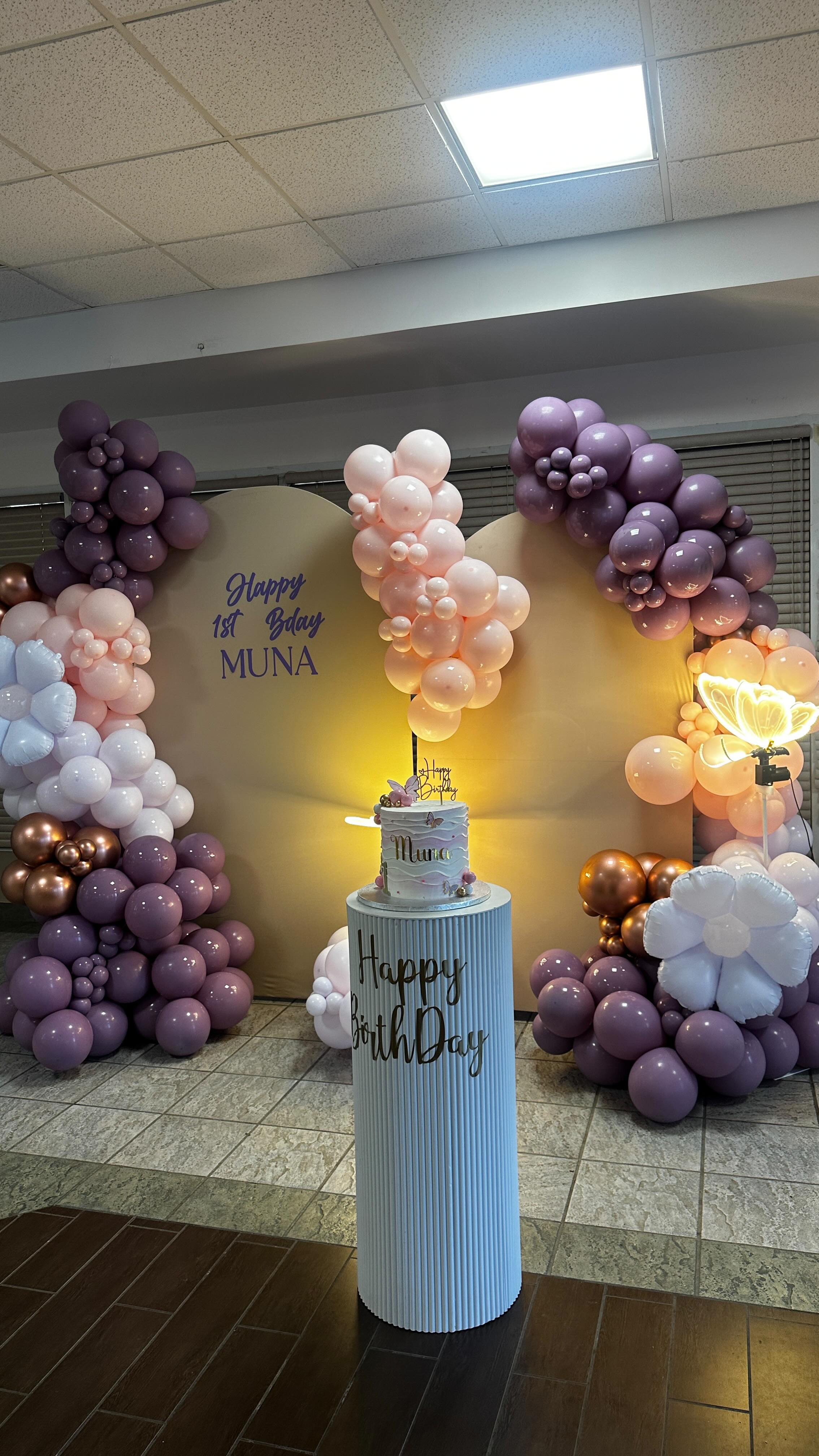 Pastel pink and white balloon installation framing a Baby Muna backdrop and celebration cake.