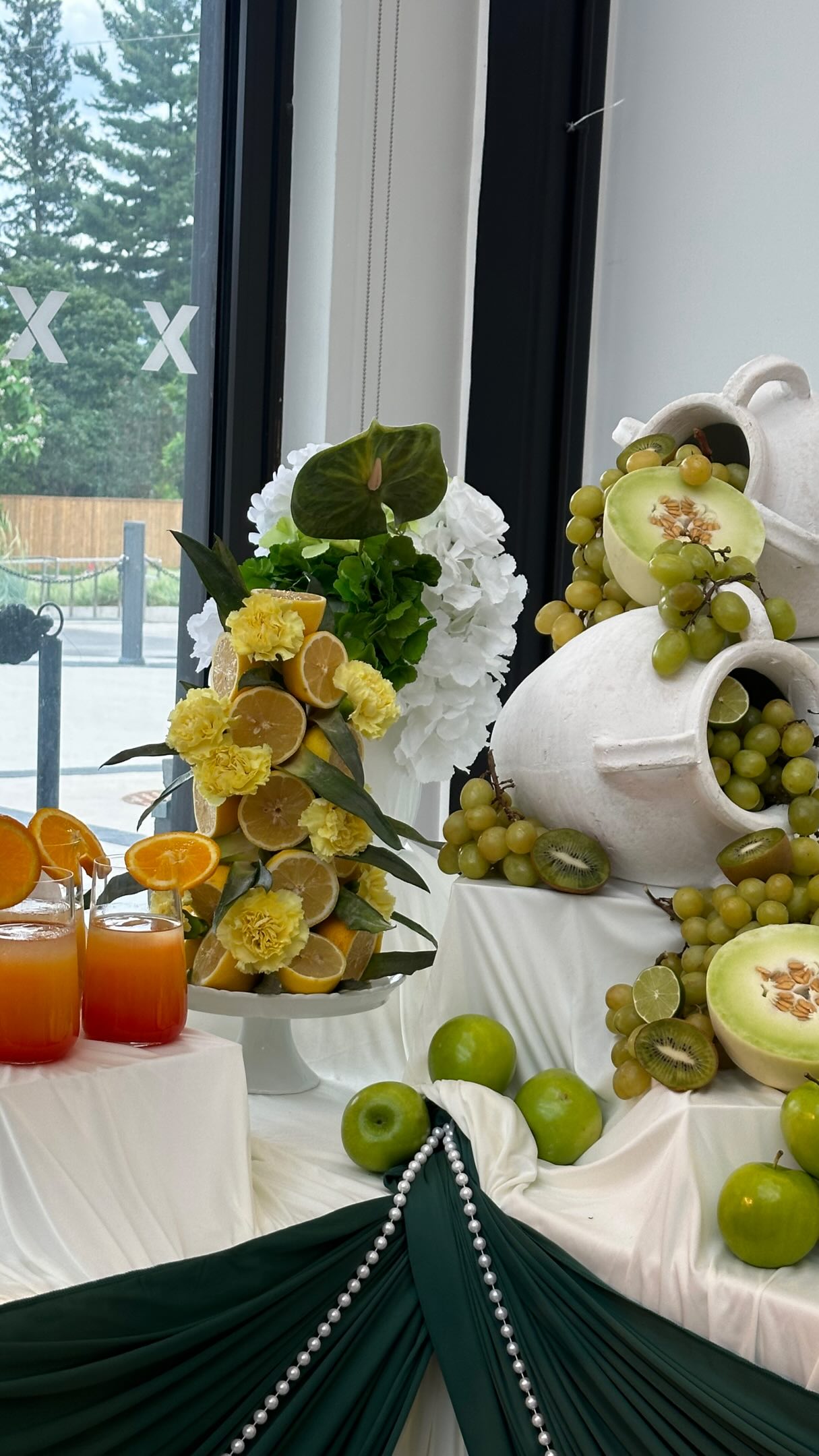 Sculptural fruit, floral, and food display arranged across curved white plinths.