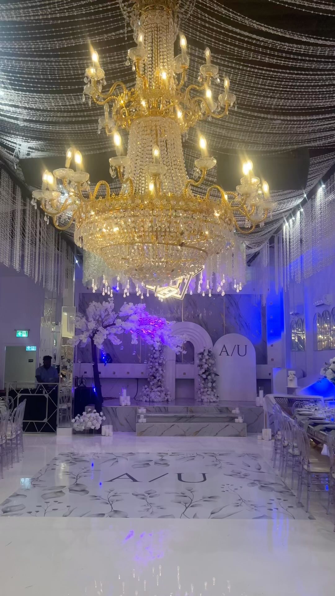 Wedding reception with white floral arrangements, gold chairs, candlelit tables, and a monogrammed white dance floor.